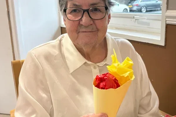 A smiling resident holding a bouquet of paper flowers