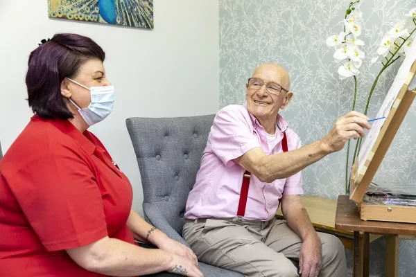 A resident painting at an easel with a member of the care team
